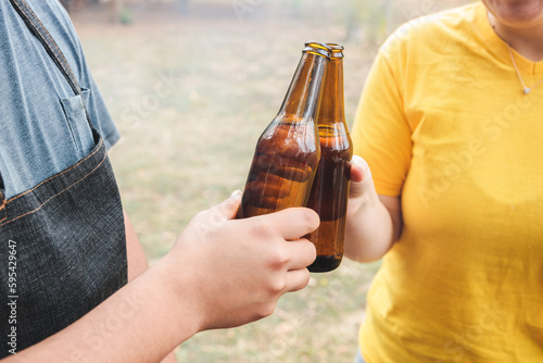 Close up of an unrecognizable young latin couple making a toast with beers at the countryside.