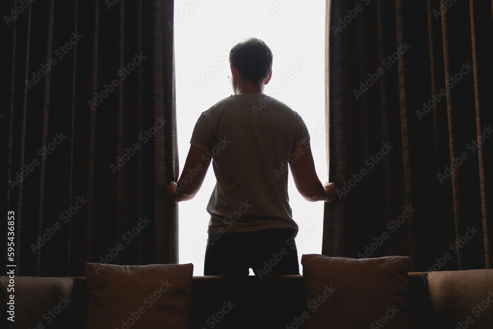 Asian man closing the curtain while watching the view out of the window. Asian man closing the curtain while watching the view out of the window.