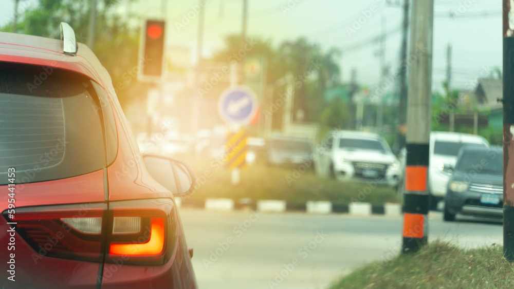 Abstract and blurred rear side of red car stop by traffic red light control. Car open trun on brack light. Cars across the street queue to drive forward. Environment of trees and country in Thailand.