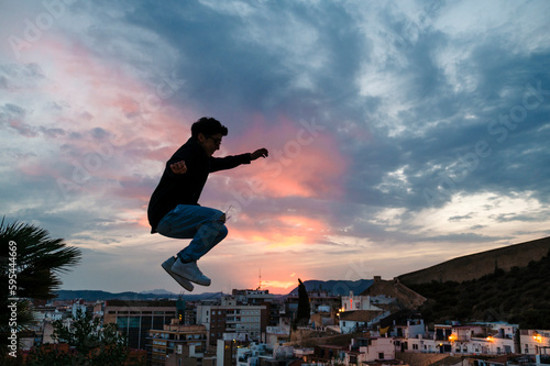 Silhouette of a person jumping outdoors with the sunset sky on background.