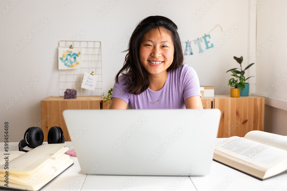 Happy, smiling teen asian female college student studying at home, doing homework using laptop looking at camera. Happy, smiling teen asian female college student studying at home, doing homework using laptop looking at camera.