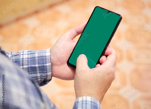 two hands holding a smartphone  with green screen with thumb finger touching the screen. Selective focus