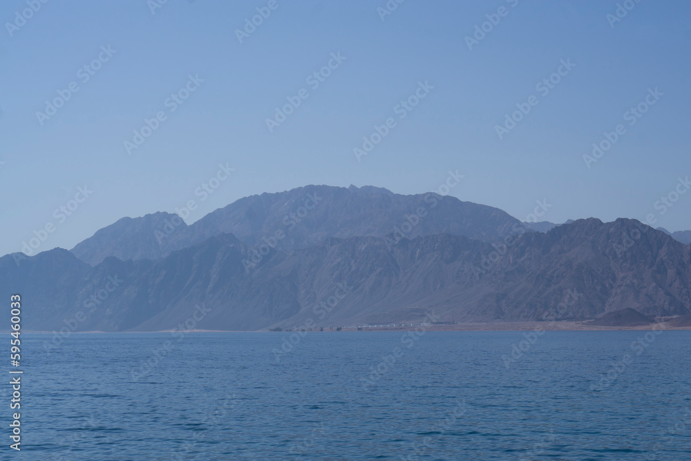 Yachts and boats moored in a sea harbor of Sharm El-Sheikh, view on a coast with panorama of mountains and lighthouse. Mountain landscape with tourist cruise boats near the Ras-Mohammed Reserve. Yachts and boats moored in a sea harbor of Sharm El-Sheikh, view on a coast with panorama of mountains and lighthouse. Mountain landscape with tourist cruise boats near the Ras-Mohammed Reserve.