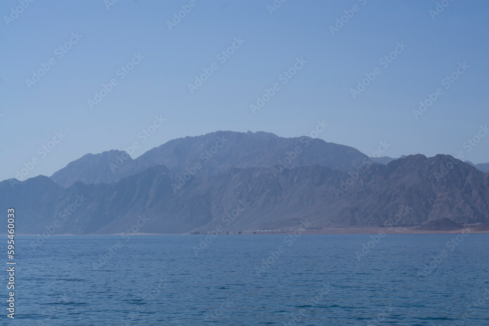 Yachts and boats moored in a sea harbor of Sharm El-Sheikh, view on a coast with panorama of mountains and lighthouse. Mountain landscape with tourist cruise boats near the Ras-Mohammed Reserve.