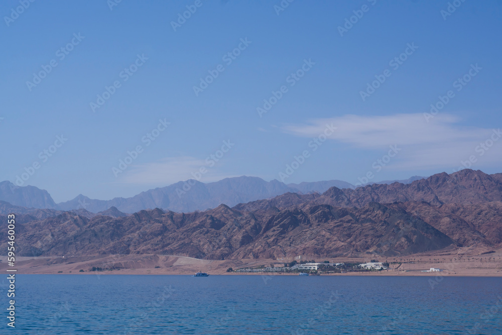 Yachts and boats moored in a sea harbor of Sharm El-Sheikh, view on a coast with panorama of mountains and lighthouse. Mountain landscape with tourist cruise boats near the Ras-Mohammed Reserve.
