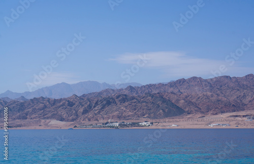 Fototapeta Naklejka Na Ścianę i Meble -  Yachts and boats moored in a sea harbor of Sharm El-Sheikh, view on a coast with panorama of mountains and lighthouse. Mountain landscape with tourist cruise boats near the Ras-Mohammed Reserve.