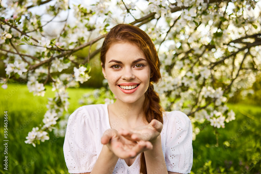 openly smiling woman against the backdrop of a flowering tree stretches her palms to the camera openly smiling woman against the backdrop of a flowering tree stretches her palms to the camera