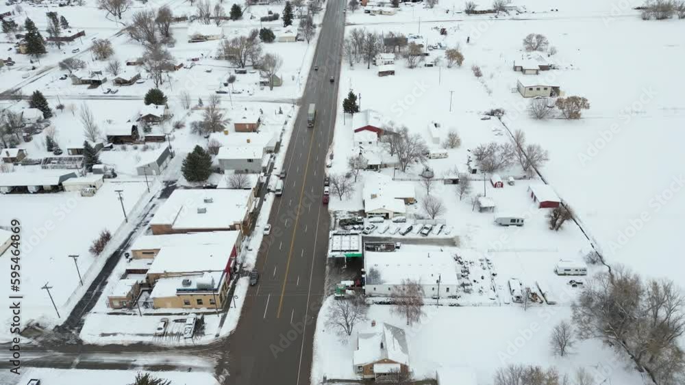 Small town under blanket of new snow with only the main highway clear. Cars and semi truck driving the road through this small rural town-Aerial pull back Small town under blanket of new snow with only the main highway clear. Cars and semi truck driving the road through this small rural town-Aerial pull back