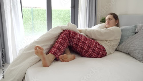 Young woman feeling cramp in leg lying in bed and massaging feet. Concept of injury, health problems, pain and trauma