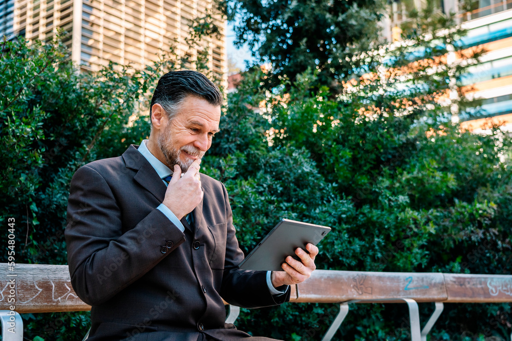 Smiling businessman browsing tablet on bench in park Smiling businessman browsing tablet on bench in park