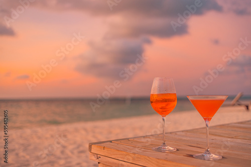 Red orange drinks with blur beach and sunset in background. Relaxing outdoor beach party, leisure lifestyle concept. Wooden table of luxurious tropical beach resort restaurant with beautiful sunset