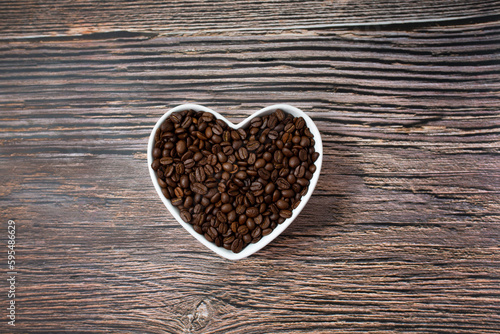 Coffee heart made of coffee beans on wooden background. Coffee in a heart-shaped bowl. Brown heart. Love coffee concept. Copy space. Top view.