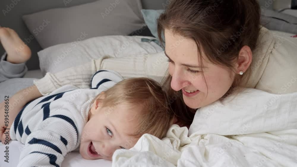 Young loving mother embracing her cute toddler son lying in bed at morning. Concept of family happiness, relaxing at home, having fun in bed, parent and cheerful kids. Young loving mother embracing her cute toddler son lying in bed at morning. Concept of family happiness, relaxing at home, having fun in bed, parent and cheerful kids.
