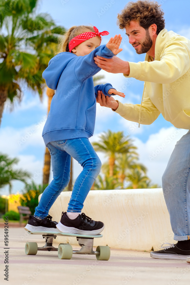 Father or private skateboard instructor teaching learn toddler daughter to ride skateboard. parental , guidance paranting ,skateboarding class, vertical,family weekend, copy space