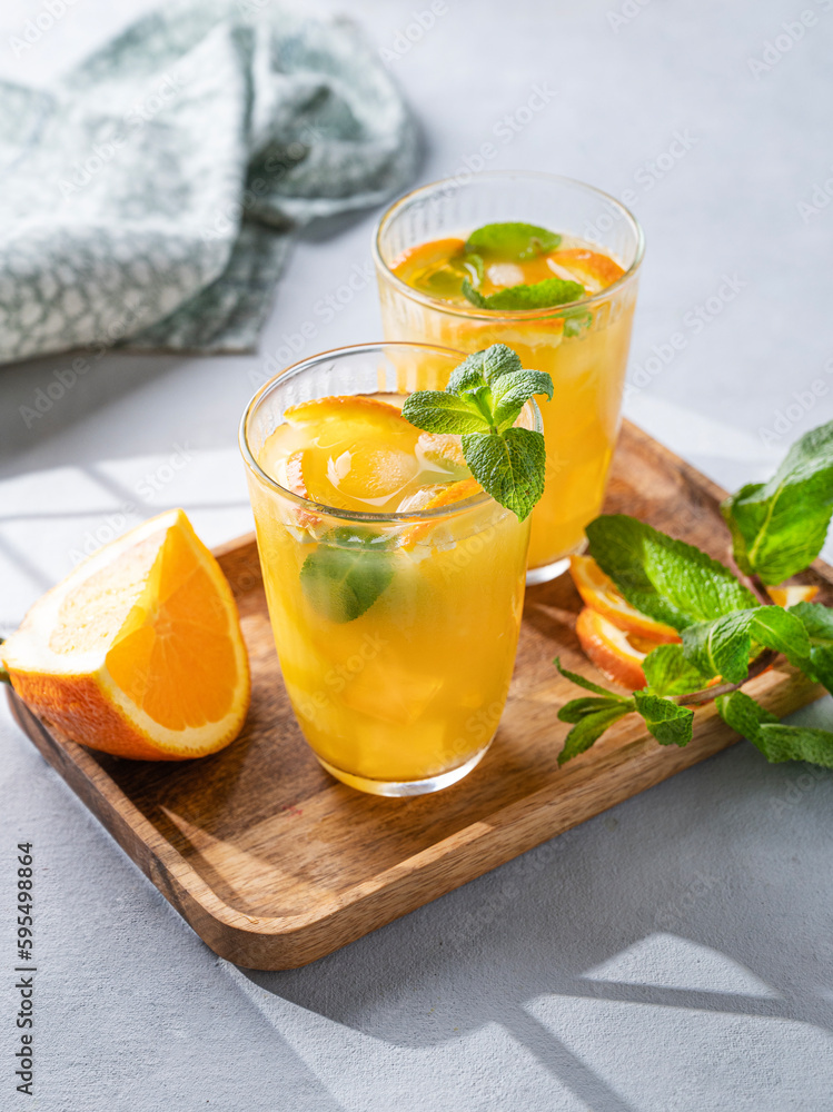 Freshly squeezed juice in a glass with fresh oranges, mint and ice on a light background with metallic tube and shadow. Healthy citrus detox drink for breakfast. Freshly squeezed juice in a glass with fresh oranges, mint and ice on a light background with metallic tube and shadow. Healthy citrus detox drink for breakfast.
