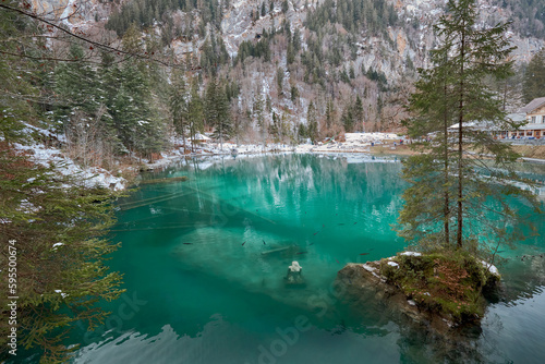 Small lake of turquoise waters in a snowy environment, known as Blausee lake in Switzerland.