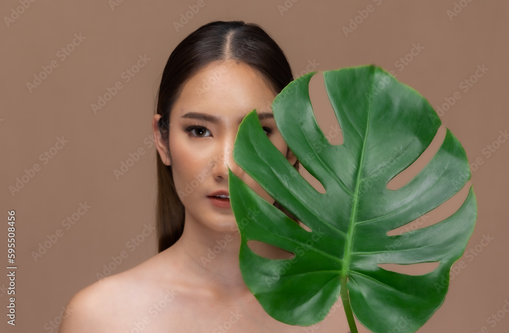 Beautiful Asian woman touching eyebrow smile with clean and fresh skin Happiness on Beige background.Beauty portrait of charm young girl with green plant leaf isolated . Beautiful Asian woman touching eyebrow smile with clean and fresh skin Happiness on Beige background.Beauty portrait of charm young girl with green plant leaf isolated .