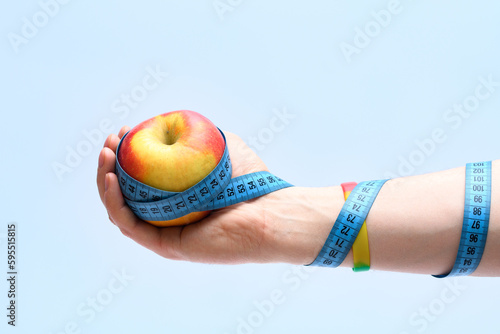 Jabłko trzymane w dłoni oplątanej taśmą krawiecką do pomiaru obwodów 
