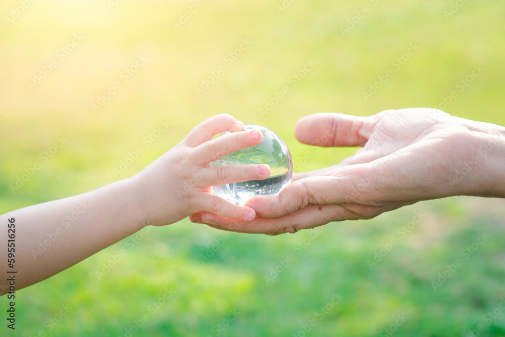 Adult person passes crystal ball to baby hand a healthy ecology to a new generation. Healthy ecology of the planet Earth. A healthy future for our generation. green glass background. Save the world. - obrazy, fototapety, plakaty 
