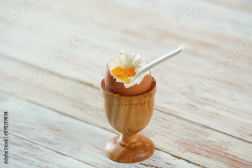 Soft-boiled egg in wooden egg cup showing runny yellow yolk with matching white ceramic spoon.