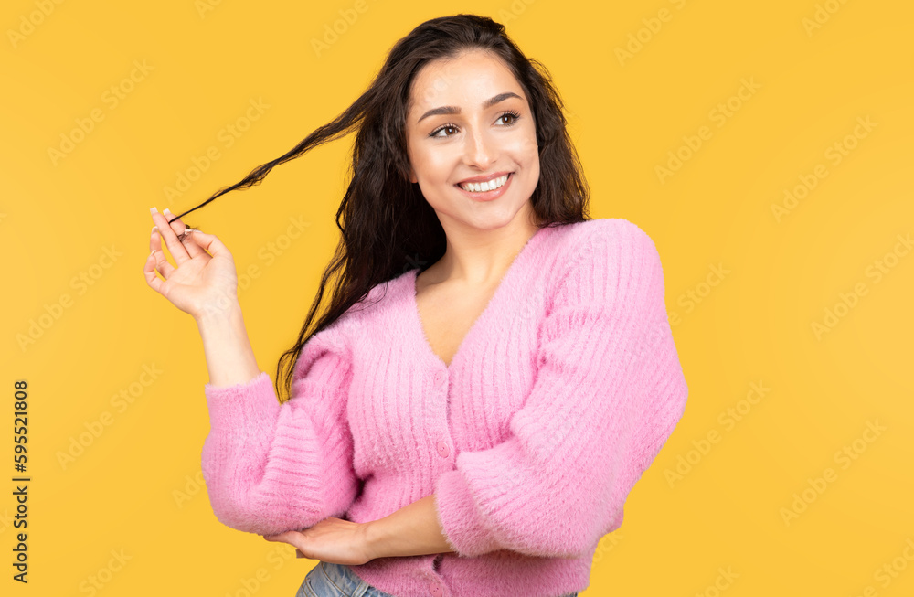 Cheerful millennial arab lady in casual holding hair, flirting, looking at empty space isolated on yellow background Cheerful millennial arab lady in casual holding hair, flirting, looking at empty space isolated on yellow background