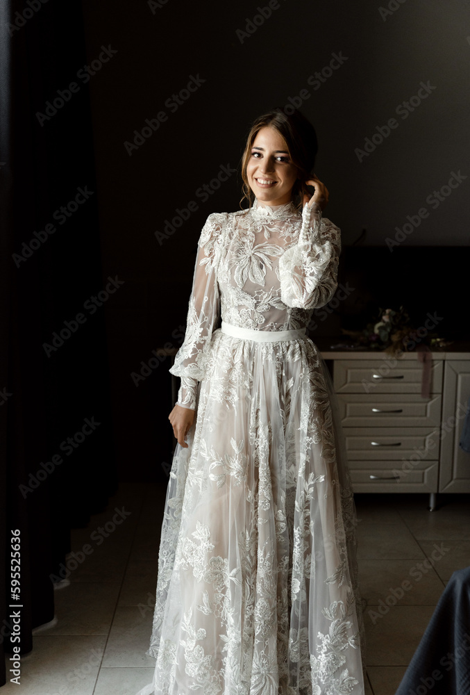 a positive bride in a beautiful wedding dress with lace is in a hotel room and is waiting for a meeting with the groom. beauty wedding day.