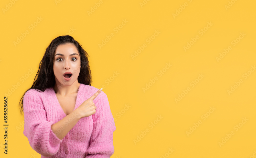 Glad shocked millennial arab woman in casual with open mouth pointing finger at copy space Glad shocked millennial arab woman in casual with open mouth pointing finger at copy space