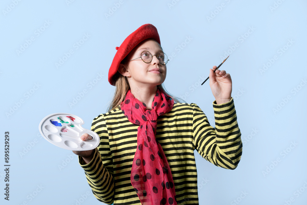 Fototapeta premium Girl with a palette of colors in a bright red beret and with a brush on a light blue background. Young artist