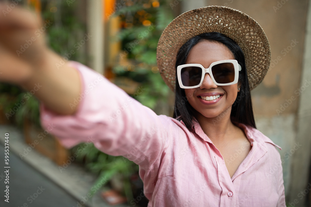 Video call, shooting travel blog. Happy young millennial black female tourist in hat and sunglass taking selfie