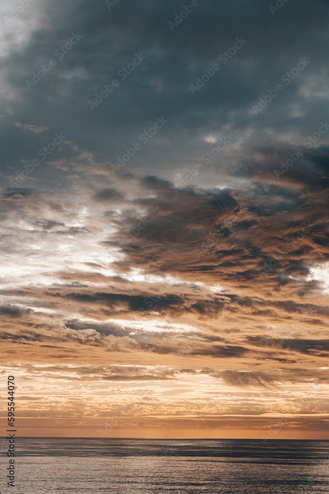Fototapeta premium Last rays of the sun illuminate clouds flying across the sky and the reflection from the sea illuminates the surrounding cliffs. Harmony of colours. Dreamscape. Sunset in the Algarve region, Portugal