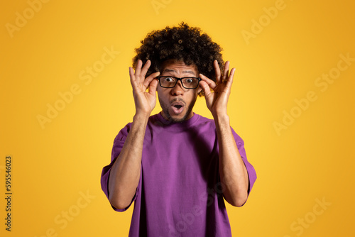 Surprise adult african american curly man in purple t-shirt with open mouth takes off glasses