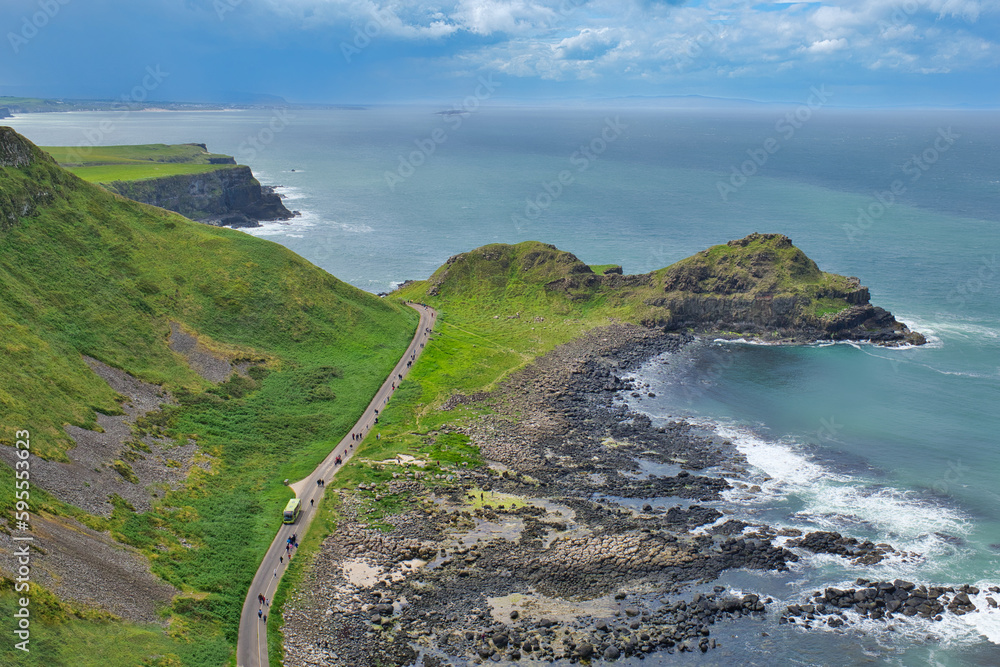A bird's-eye Aerial view of a bus and a pedestrian path leading to the Giant's Causeway, with beautiful ocean scenery and blue sky can be seen from the cliff trails in Northern Ireland, UK.