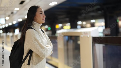 Portrait of Asian woman tourist waiting for the train at railway station at night. Attractive girl traveler enjoy urban lifestyle travel in the city by railroad transportation on holiday vacation.