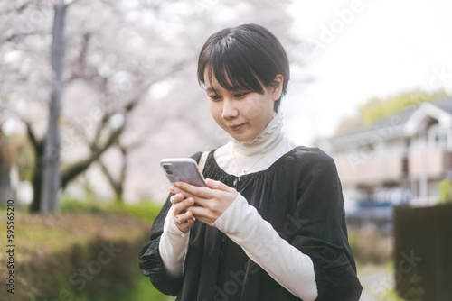 Young adult asian japanese woman using smartphone at outdoor park spring season background with copy space