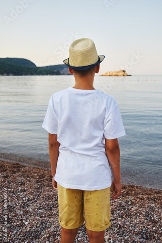 Teenage boy in a straw hat and a white t-shirt looks into the sea. Concept of acation and travel.