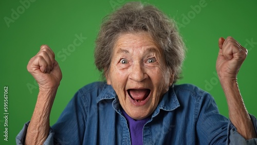 Obraz na plátně Closeup portrait of toothless elderly senior old woman with wrinkled skin and grey hair getting great happy with success winner isolated on green screen background