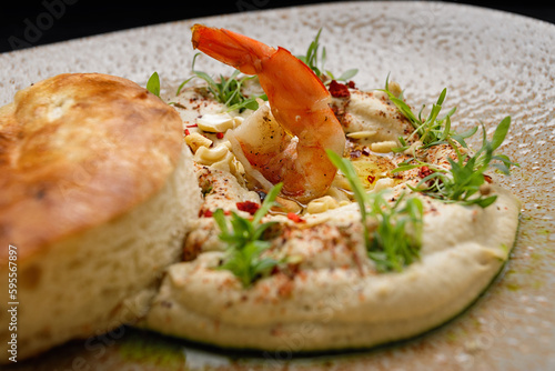 Hummus with shrimp, peanuts, chickpeas and a bun, on a plate