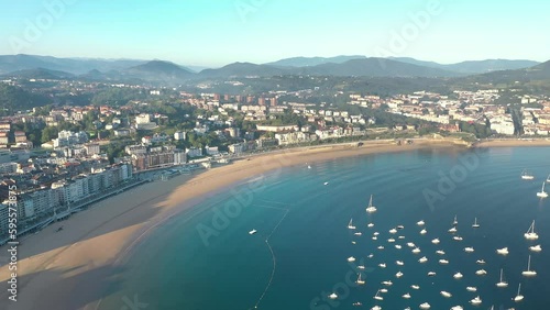 Aerial perspective of San Sebastian - Donostia City. View of city center and famous beach La Concha at sunrise. Beautiful warm colours and long shadows. Sun in the left corner. Drone going backword photo