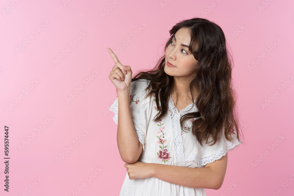 Young smiling Asian woman pointing finger sideways to copy space in pink color background. Young smiling Asian woman pointing finger sideways to copy space in pink color background.