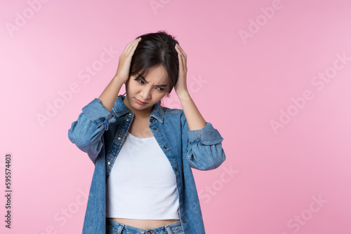 Young Asian woman is suffering from a severe headache, pressing her hand to her temples and frowning to relieve pain, with a helpless expression on her face.
