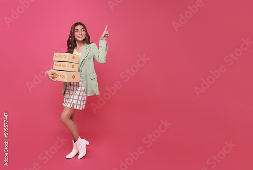 Happy Asian woman smiling holding package parcel box pointing finger isolated on pink copy space background.