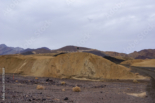 Man with scenic view Badlands of Zabriskie Point, Furnace creek, Death Valley National Park, California, USA. Erosional landscape of multi hued Amargosa Chaos rock formations, Panamint Range in back
