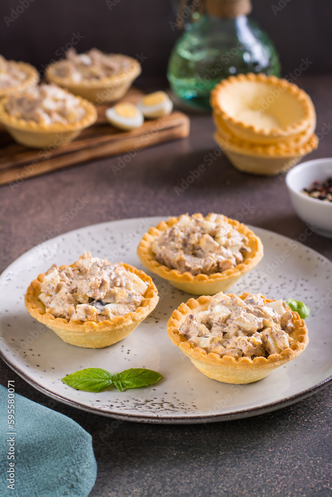 Appetizing tartlets with egg, canned tuna and onion salad on a plate on the table vertical view