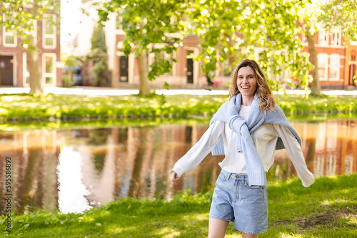 Portrait of beautiful woman smiling and turn around in park at sunny day. Outdoor portrait of a smiling curly blonde girl. Happy cheerful girl laughing at park wear sweater  white longsleeves  shorts