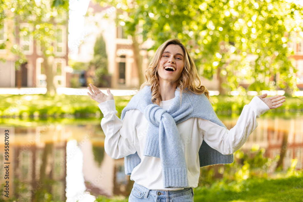 Beautiful woman smiling and look at camera at park at sunny day. Outdoor portrait of a smiling curly blonde girl. Happy cheerful girl laughing at park, spread her hands and show toothy smile. Beautiful woman smiling and look at camera at park at sunny day. Outdoor portrait of a smiling curly blonde girl. Happy cheerful girl laughing at park, spread her hands and show toothy smile.
