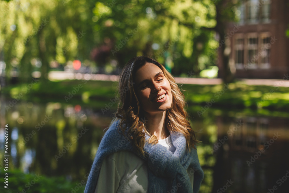 Beautiful woman smiling and look at camera at park at sunny day. Outdoor portrait of a smiling curly blonde girl. Happy cheerful girl laughing at park, look fashion and show toothy smile. Closed eyes. Beautiful woman smiling and look at camera at park at sunny day. Outdoor portrait of a smiling curly blonde girl. Happy cheerful girl laughing at park, look fashion and show toothy smile. Closed eyes.