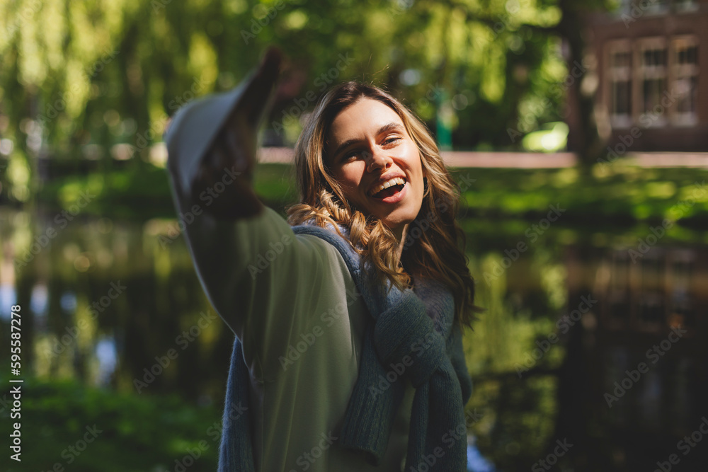 Beautiful woman smiling and look at camera at park. Outdoor portrait of a smiling curly blonde girl raise hand to camera. Happy cheerful girl laughing at park, look fashion and show toothy smile. Beautiful woman smiling and look at camera at park. Outdoor portrait of a smiling curly blonde girl raise hand to camera. Happy cheerful girl laughing at park, look fashion and show toothy smile.