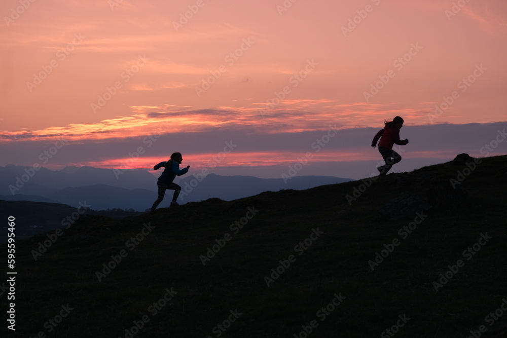 children running up the mountain fell with an amazing sunset