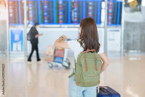 Young woman with bag and luggage checking flight time information board in international airport, before check in. Travel, Vacation, trip and Transport concept