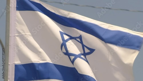 Shot of Israeli flag blowing in the wind in slow motion - State of Israel flag on pole with blue sky in background - Star of David
 photo